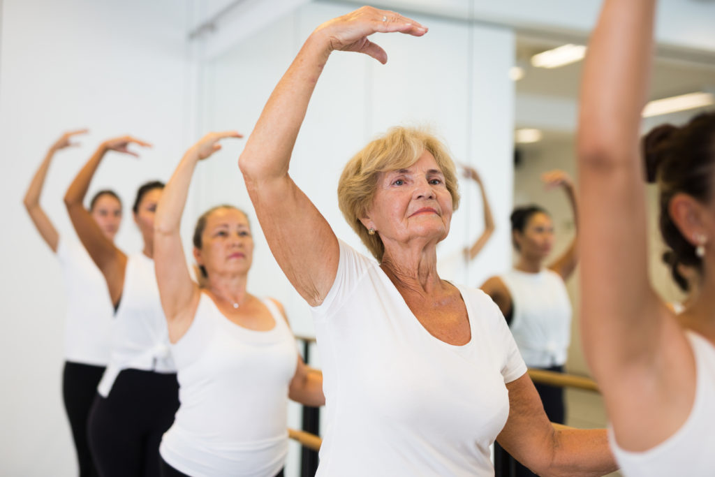older women with arm above their heads during barre fitness class